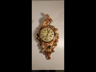 Emil N. Stockholm -seinäkello, jossa on lehtikultaus koristeissa. Korkeus 53cm ja leveys 29cm